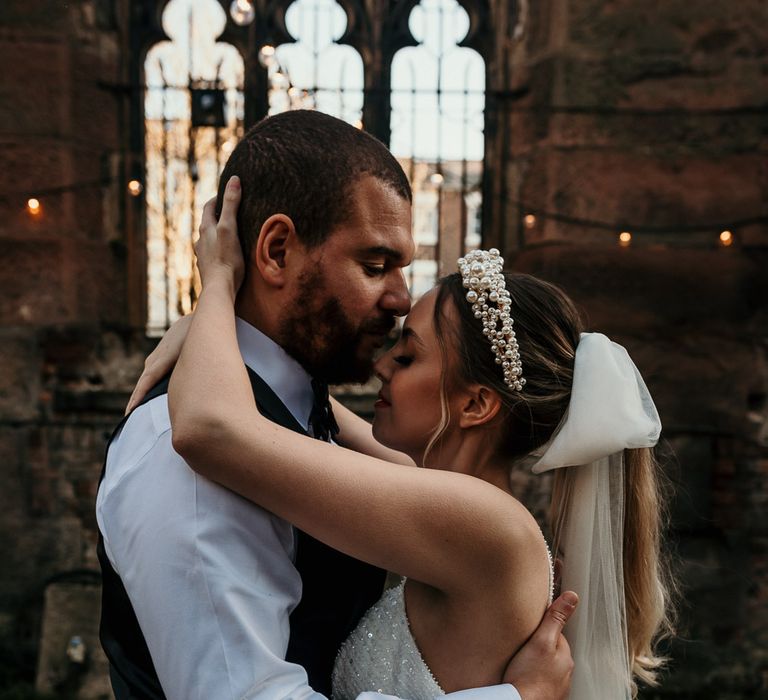 Bride with a pearl headband and bow veil embracing her husband in St Lukes Bombed Out Church in Liverpool 