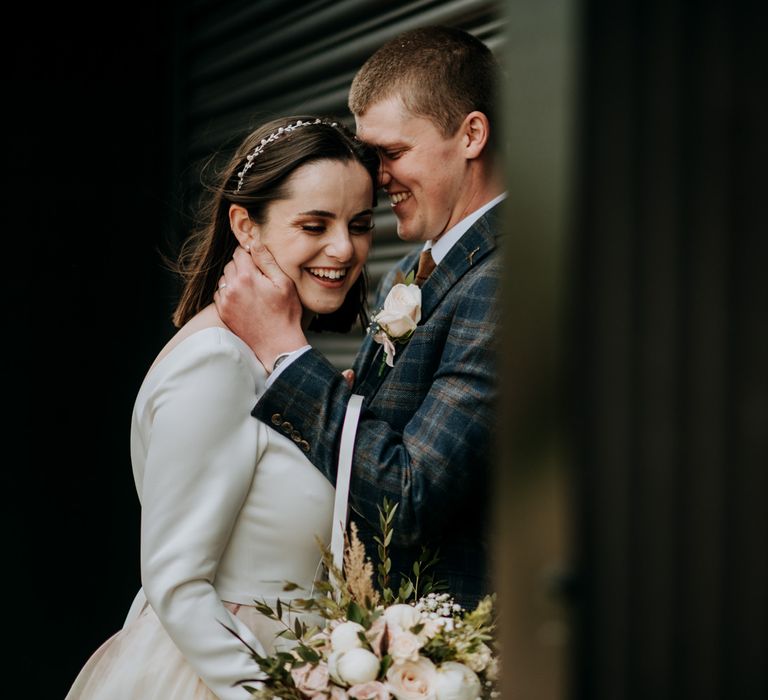 Intimate wedding party portrait with groom in a navy and brown check suit embracing his brides face with short bobbed hair in a delicate headband 