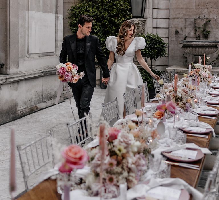 Bride and groom entering their luxury wedding reception with ghost chairs, pink taper candles and floral centrepiece decor 