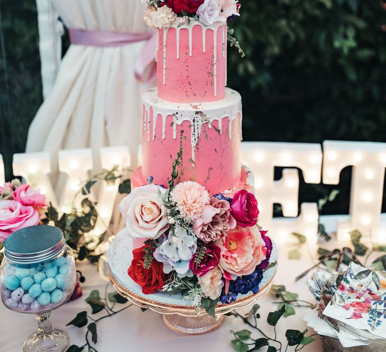 Wedding cake with pink frosting and white dripping decorated with florals