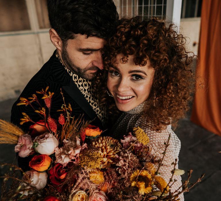 Bride with naturally curly hair and makeup with winged eyeliner holding an orange and yellow autumnal bouquet 