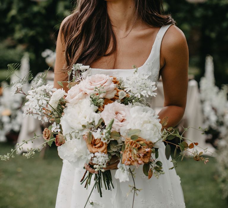 Bride with long wavy hair and natural wedding makeup holding a white, blush and orange wedding bouquet with roses, stocks and foliage 