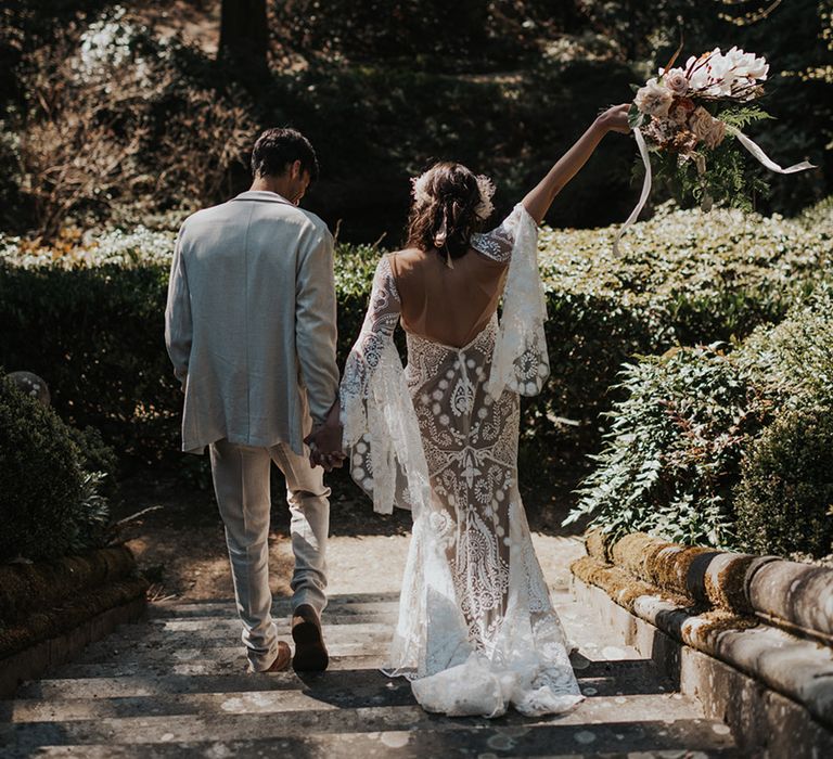 Bride in a boho wedding dress with bell sleeves and low back detail holding her bouquet in the air 