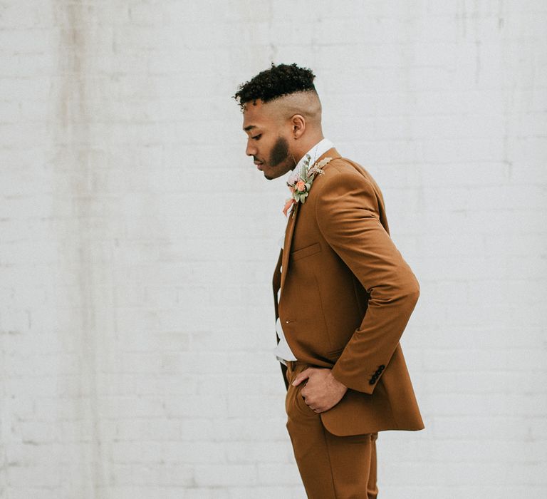 Stylish groom in a dark orange coloured wedding suit with white trainers 