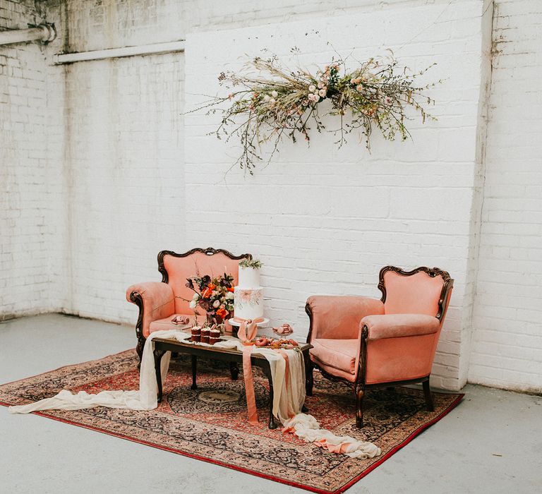 rich orange upholstered chairs standing on a wool rug with a coffee table dessert station including a painted wedding cake 