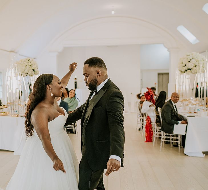 A Black couple celebrate their wedding by dancing on the dance floor. The bride wears a strapless sweetheart neckline dress and the groom wears black tie.