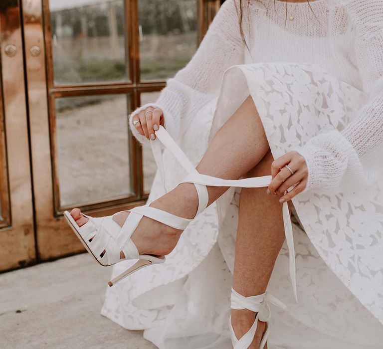 Bride putting on her Emmy London wedding shoes with ribbon ankle strap details 