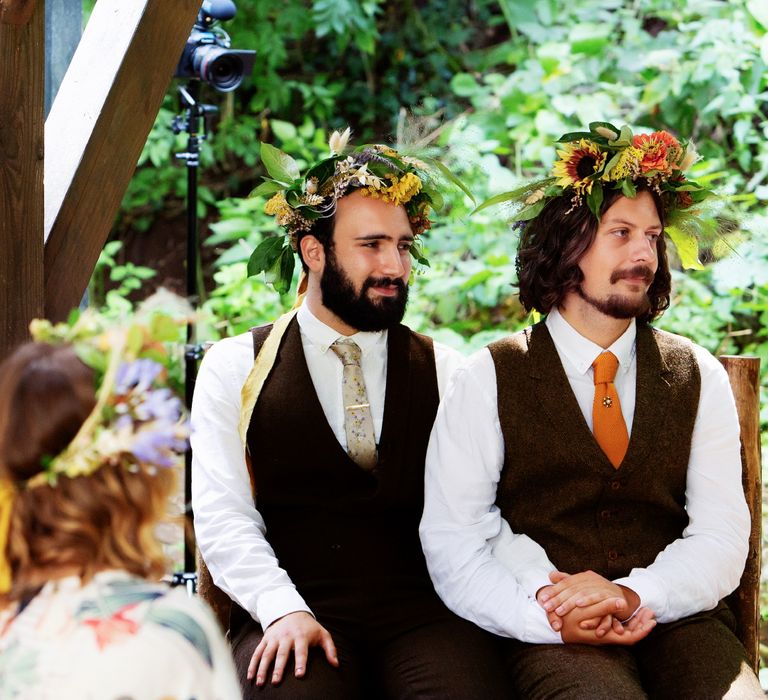 Grooms look across during wedding ceremony as they both wear brown waistcoats complete with colourful ties