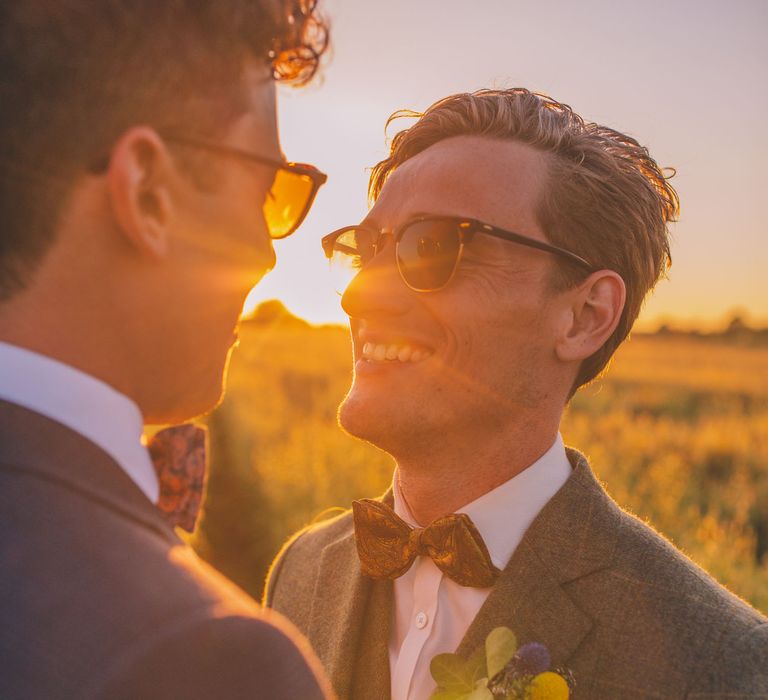 Groom looks lovingly at his groom as the sun sets behind them during golden hour portraits | Story + Colour