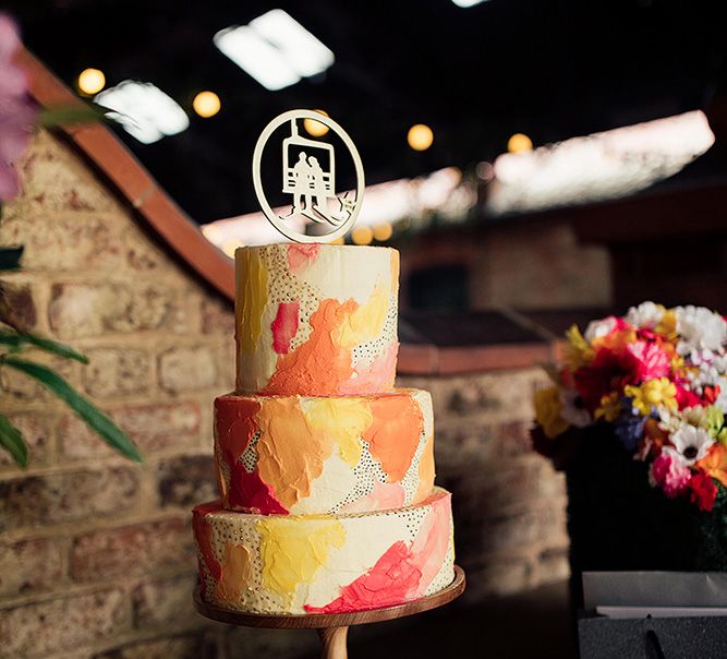 Orange yellow and red contemporary wedding cake with laser cut cake topper of couple sitting on a bench 