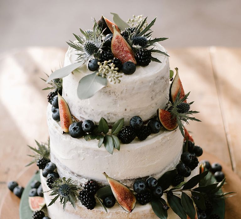 Three-tier buttercream wedding cake decorated with foliage, fruits and figs 