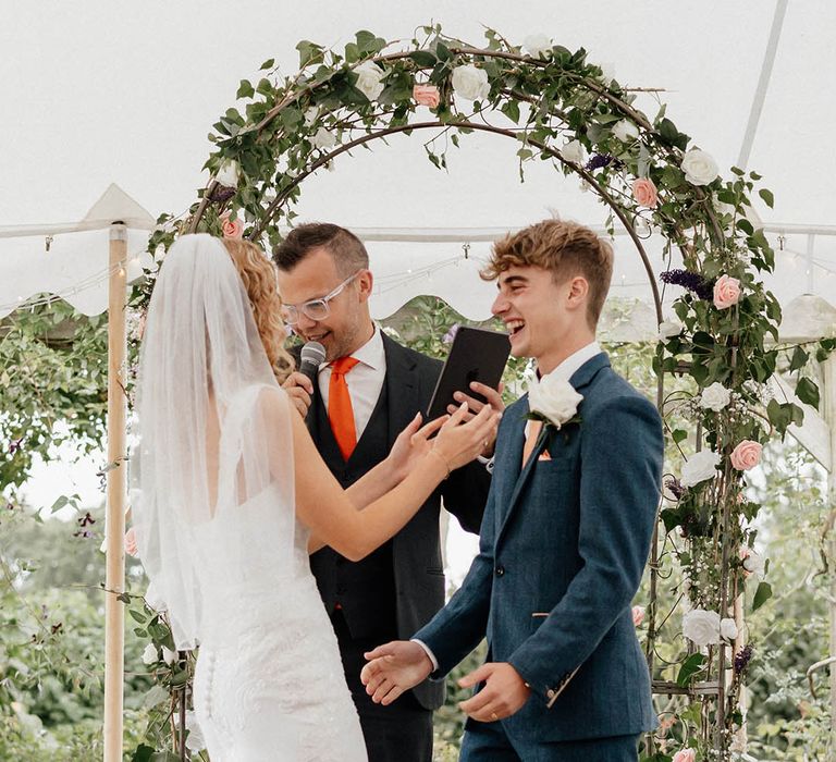 Bride & groom go to hug one another under floral archway on their wedding day in Marquee 