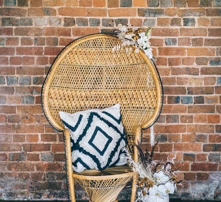 Wicker peacock chair on a wool rug with vintage suitcases, cushions and dried flower decor 