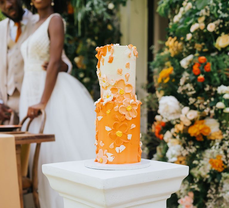 Orange and white buttercream wedding cake with petal decor at outdoor wedding 