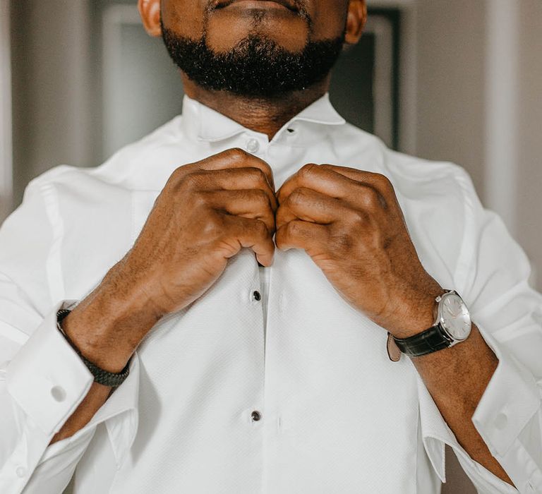 Groom does up the button of his shirt on the morning of his wedding day