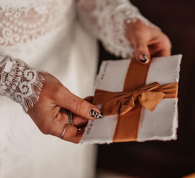 Bride with leopard print nails and lace bridal two piece dress holds vows on white paper tied with orange ribbon