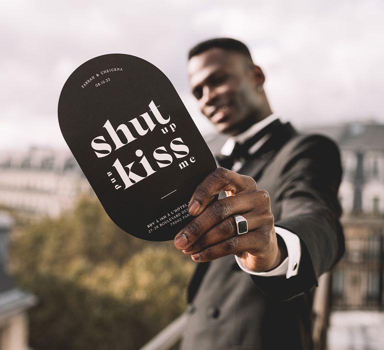 Groom in a tuxedo holding a black and white contemporary wedding invitation 