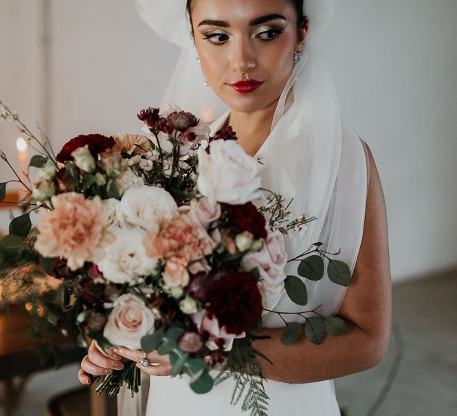 Bride holds floral bouquet whilst wearing deep lipstick