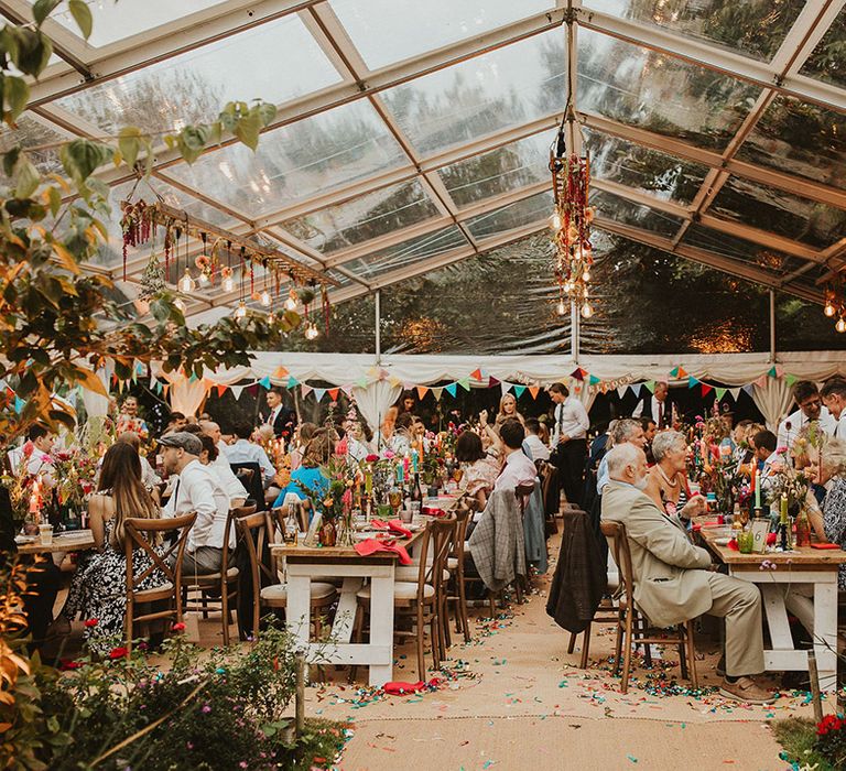 Clear marquee wedding reception with hanging light installations, bunting and foliage decor 