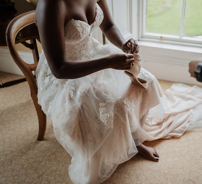 Bride puts on satin wedding heels as her embellished wedding dress drapes 