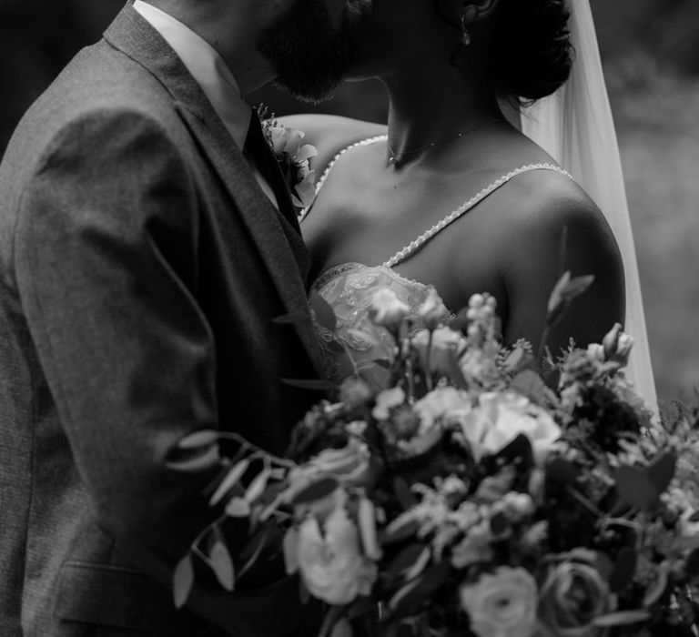 Bride & groom kiss on their wedding day outdoors as she holds floral bouquet