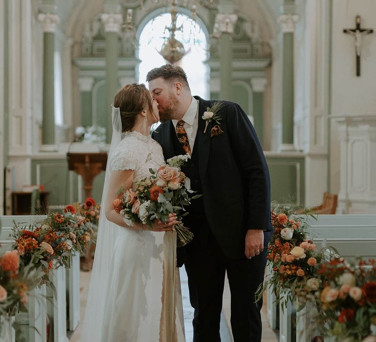 Bride and groom kiss at church ceremony with orange and blush flowers