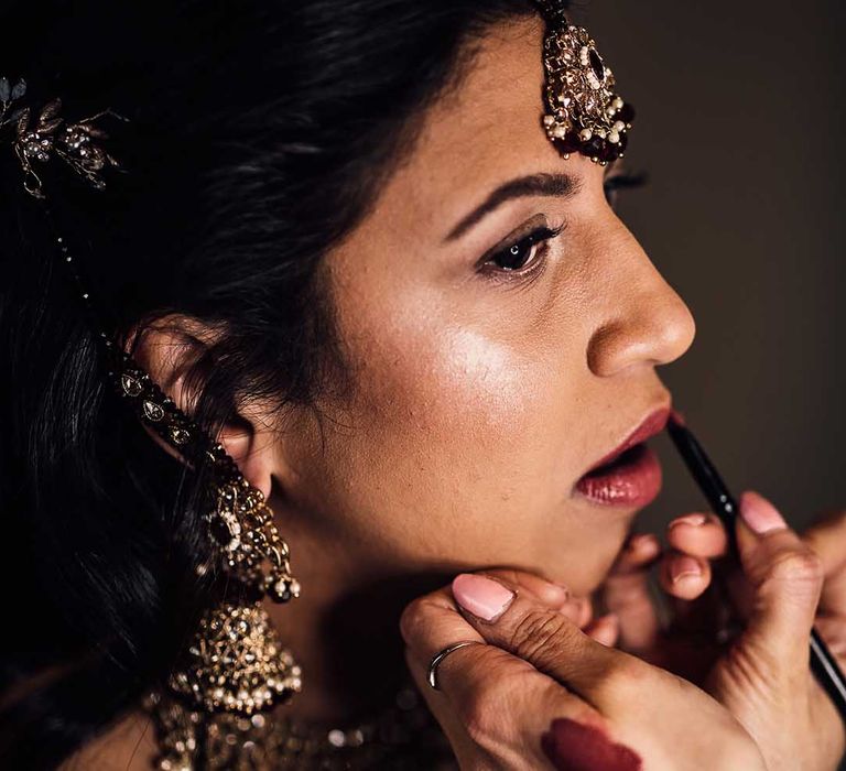 Indian bride gets make up done at her wedding wearing gold jewellery 