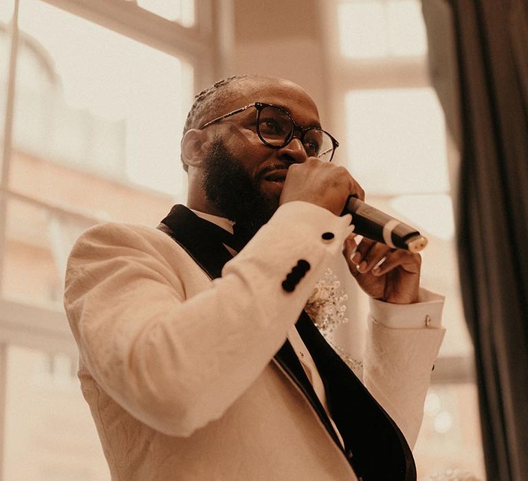 Groom in a white brocade tuxedo jacket giving his wedding speech 