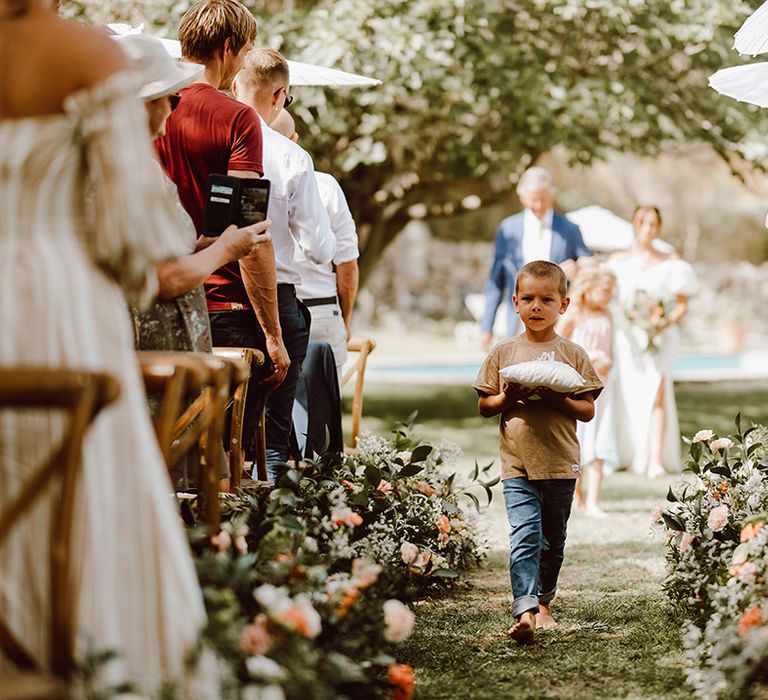 Young ring bearer in jeans walks down the aisle barefoot