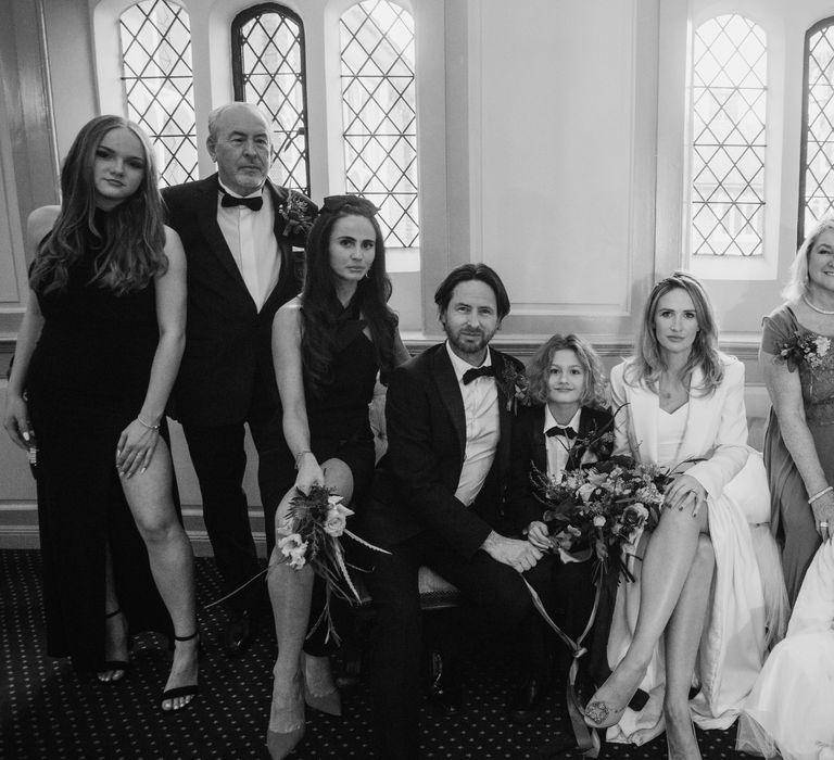 Bride & groom sit with their son and wedding guests at Gosfield Hall on their wedding day in black & white image 