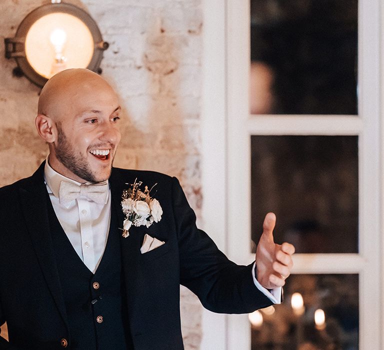 Groom in a black three-piece suit with bow tie giving his wedding speech 