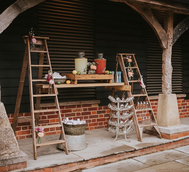 Rustic hydration station made of juices and lemonade with wooden ladders with milk bottles and flowers 