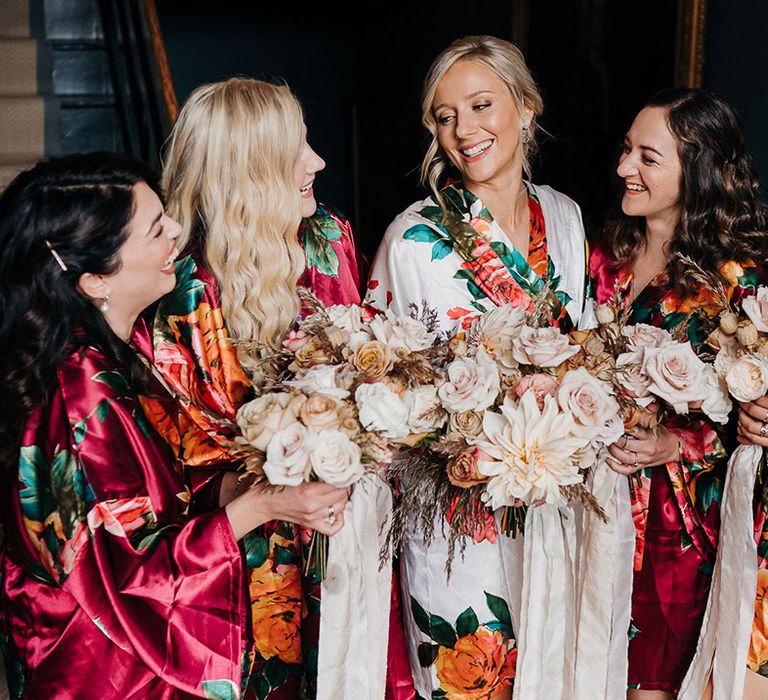 Bride and bridesmaids in matching dressing gowns stand with their bouquets tied with white ribbon