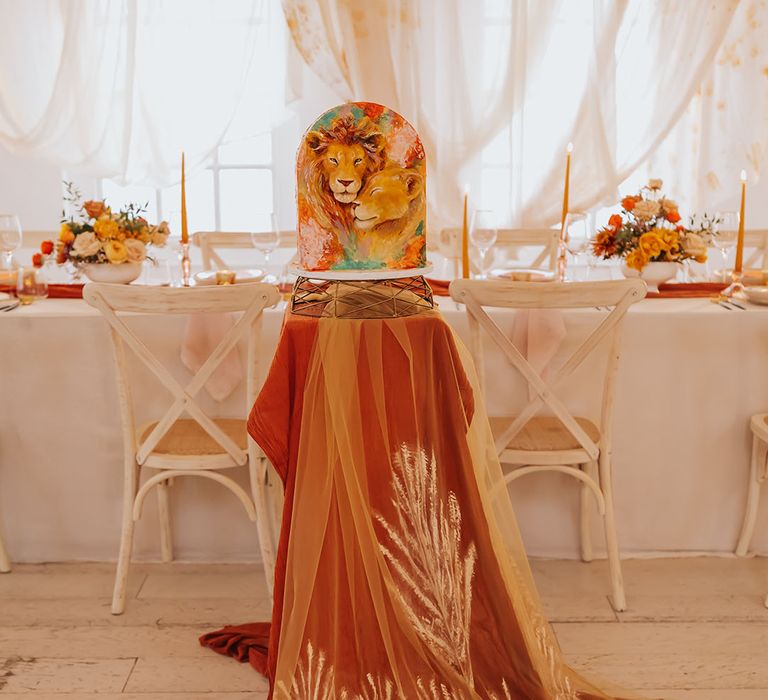 Lion wedding cake on a gold cake stand and burnt orange table cloth and patterned veil