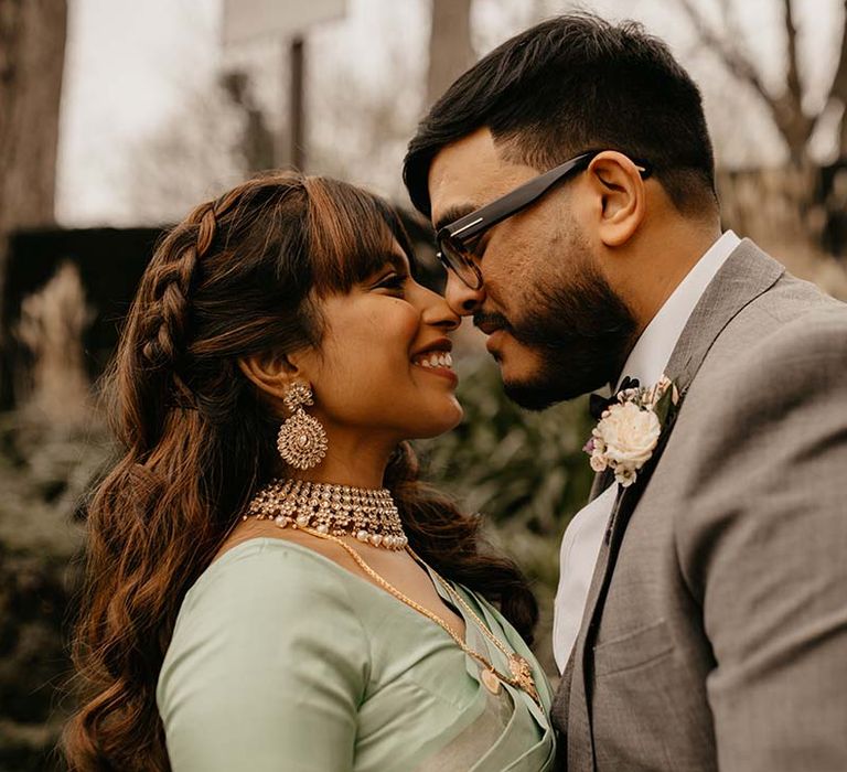 Bride in mint green saree and groom in grey suit smiling, heads touching at multicultural wedding