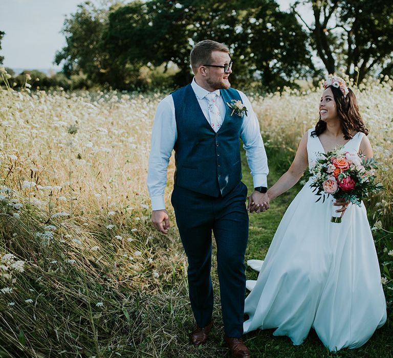 Bride and groom intertwined their fingers as they walk along together after their outdoor wedding ceremony 