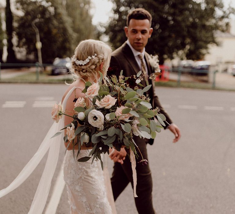 Bride in Made With Love Bridal wedding dress carrying pink, white and deep red bouquet walking with groom in brown suit