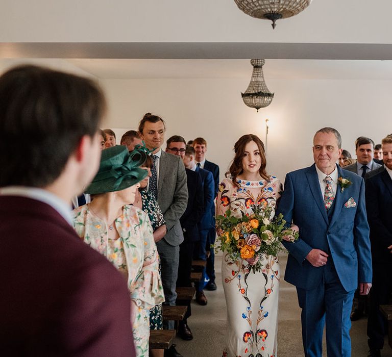 Father of the bride in dark blue three piece suit with bride in Temperley Bridal dress heads towards the groom in burgundy suit