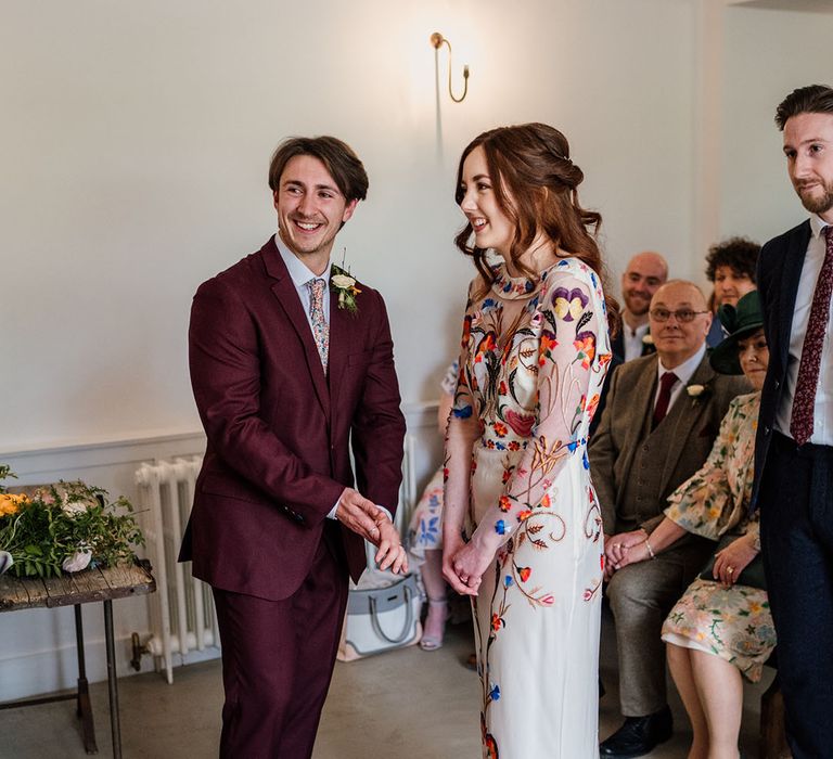 Bride in colourful and bright wedding dress and groom in burgundy three piece suit for wedding 