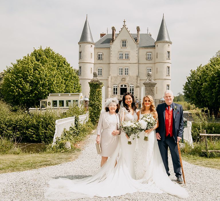 Brides in lace wedding dresses and matching red lipstick with parents outside the chateau 