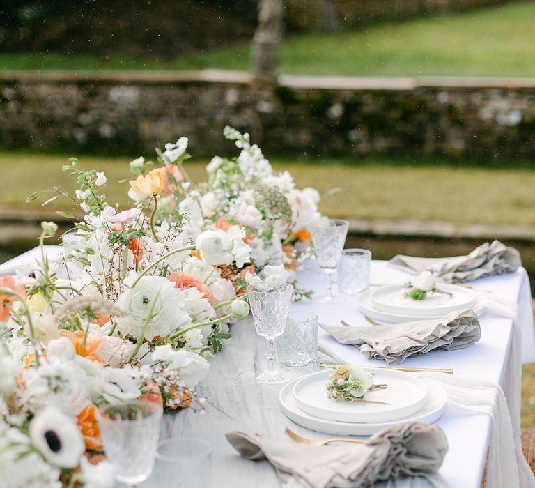 outdoor wedding tablescape with flower table runner and white place settings with buttonholes 