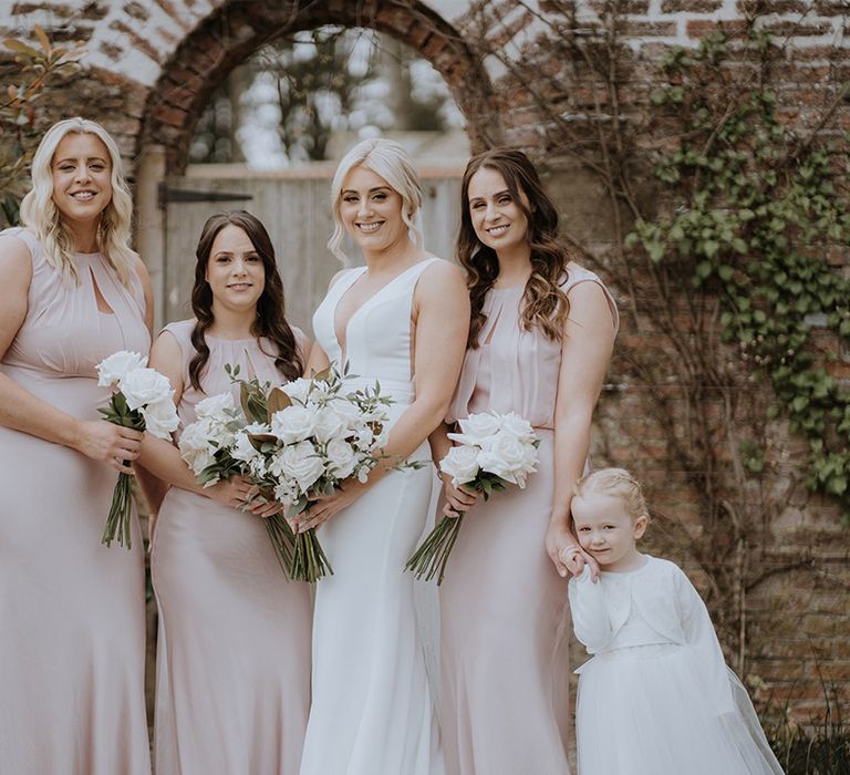 Bridesmaids in pale pink dresses with bride in Made With Love dress and flower girl in tulle dress and pearl cardigan