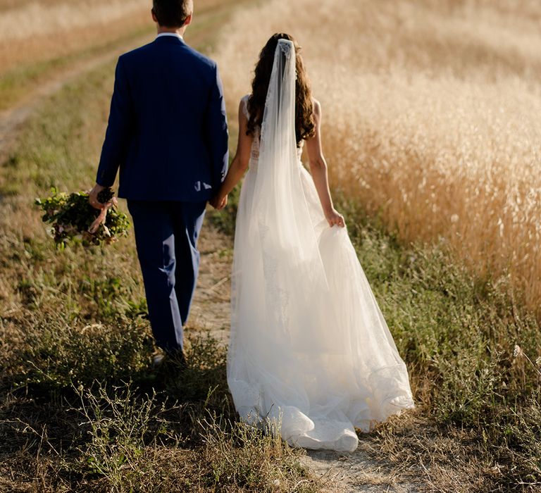 Bride & groom walk through golden fields in Tuscany 