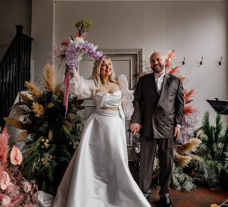 Groom in a double breasted suit with his bride in a JESUS PEIRO wedding dress holding her exotic flower bouquet in the air 