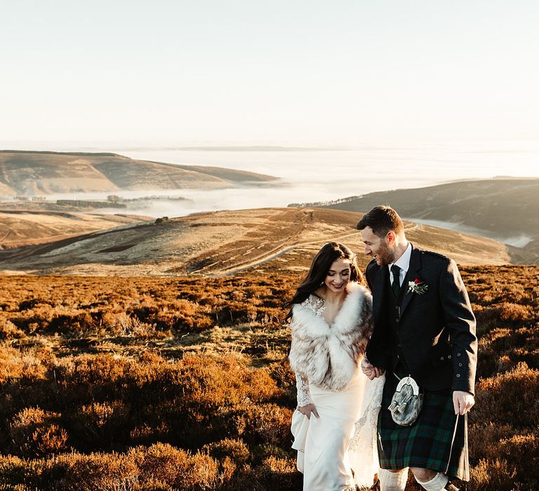 Bride & groom walk across beautiful Scottish hills during sunset on their wedding day