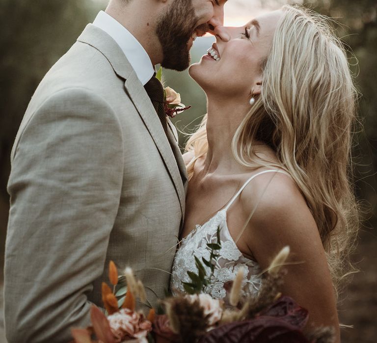 Bride & groom look lovingly at one another as bride wears Annoushka pearl drop earrings and holds colourful floral bouquet 