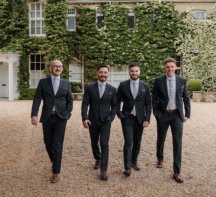 Groom walks with his groomsmen who wear matching suits complete with green ties and pocket squares 