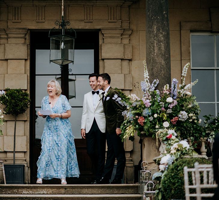 Grooms stand beside celebrant in front of Birdsall House during outdoor ceremony 