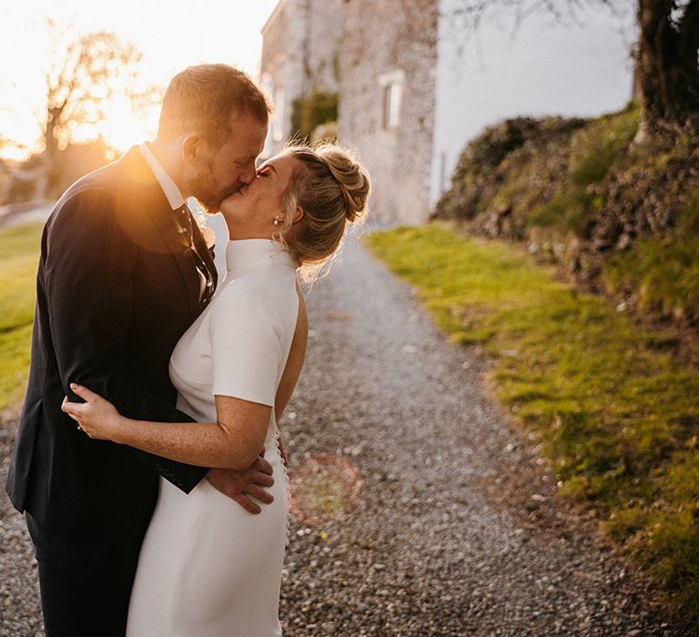 Bride and groom kiss outside the wedding venue, Launcells Barton during golden hour 