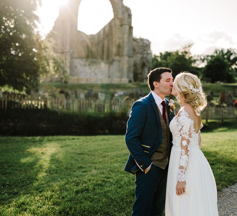 Bride wearing long sleeve lace Pronovias wedding dress kisses her groom as the sun begins to set on their wedding day